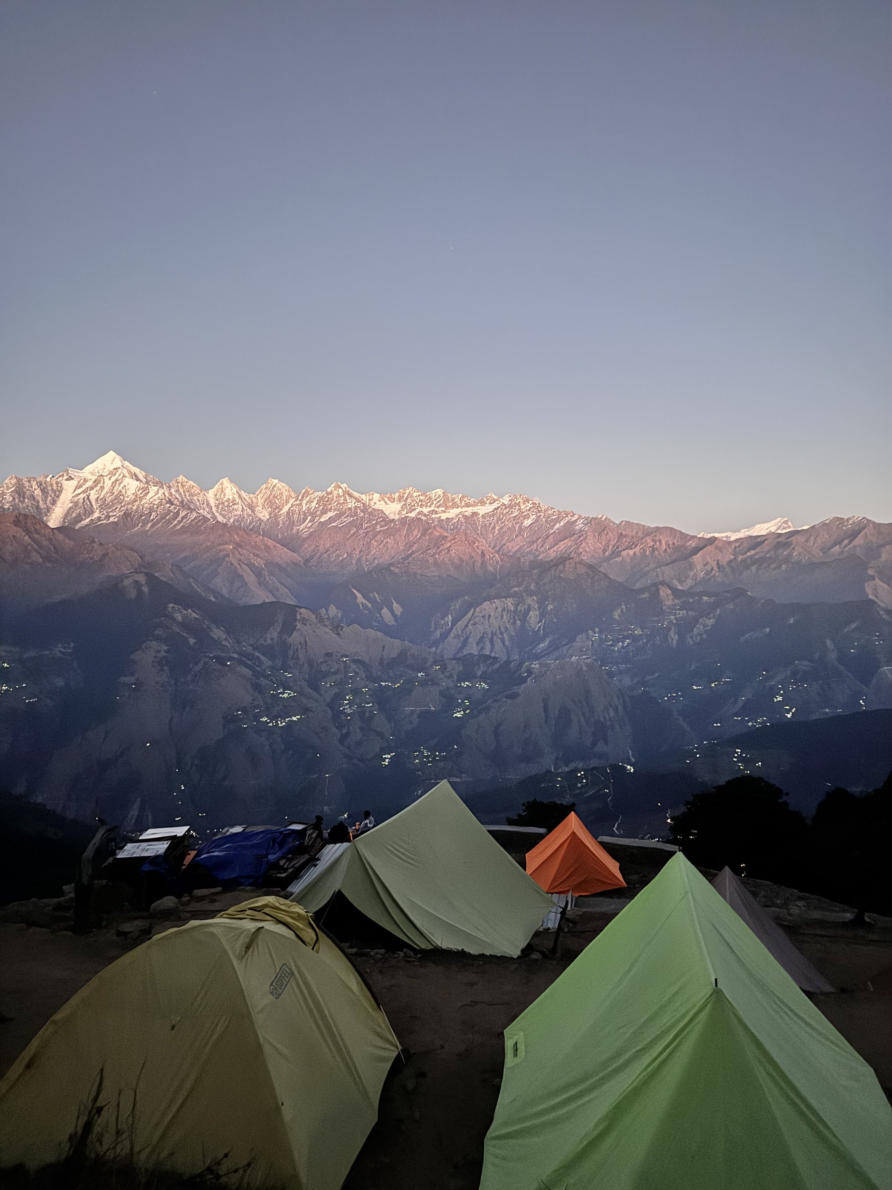 Tents at the Khaliya Top campsite at dusk, alpenglow lighting the Panchachuli range with valley lights below