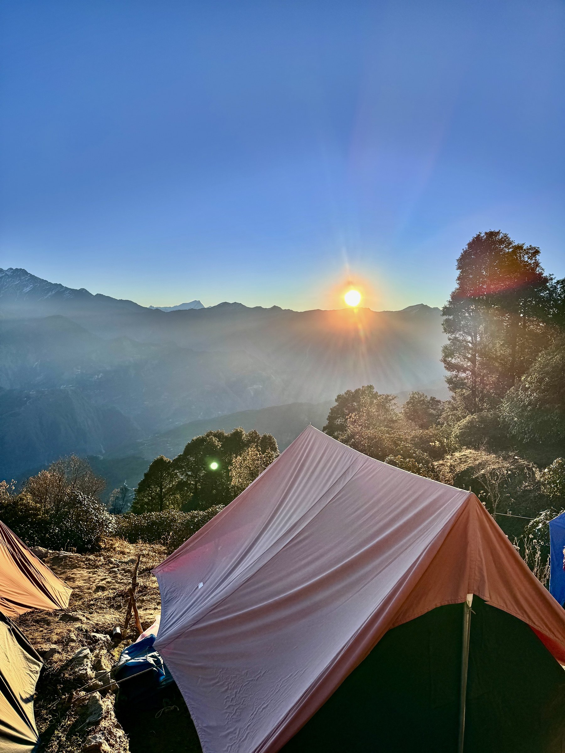 Sunrise breaking over the mountains behind a tent at Khaliya Top