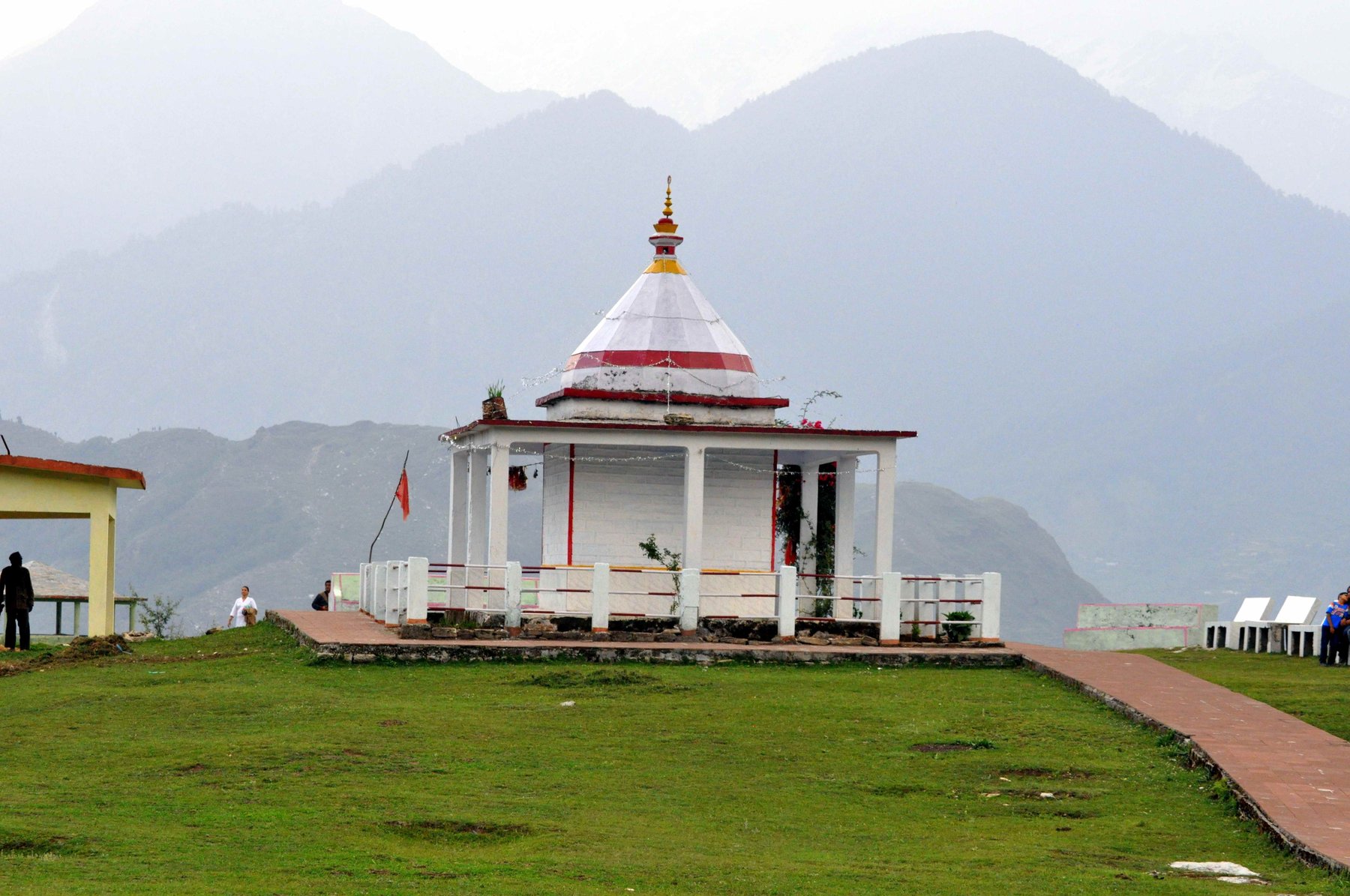 Wide view of the whitewashed Nanda Devi Temple pavilion on its viewpoint terrace, mountains behind